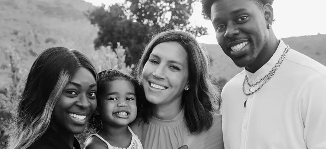A black-and-white portrait of three adults and a child with a background of trees and mountains.
