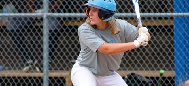 A female baseball player wearing a grey and light blue uniform prepares to hit a ball.