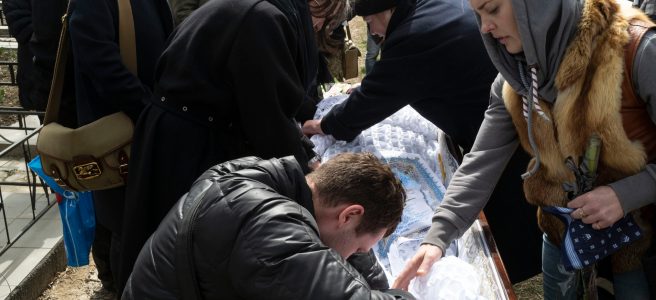 A man and woman grieve over the casket of Andrii Tanulin, a victim of the bombing in Ukraine. They are accompanied by several other mourners.