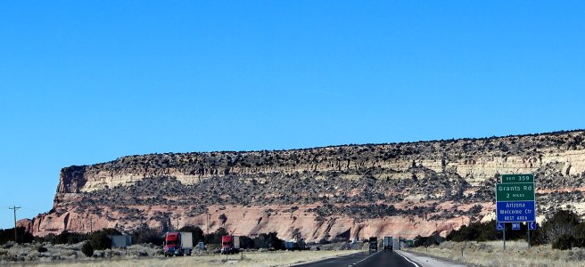 A highway in Arizona leads to a large, rocky cliffside. The signs on the highway read: "Exit 359, Grants Rd, 2 miles," and "Arizona Welcome Center Rest Area."