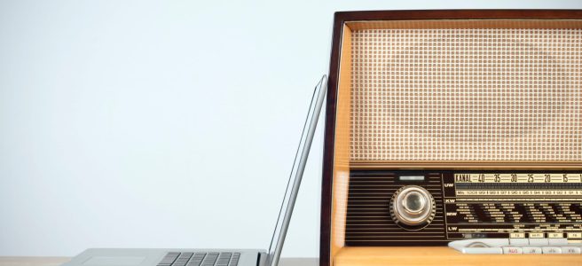 An open laptop leans against an old-style radio atop a table.