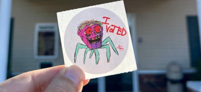 A round “I voted” sticker shows a childish drawing of a green-legged spider figure with a smiling human head. The face is in shades of purple with big red eyes and multicolor teeth.