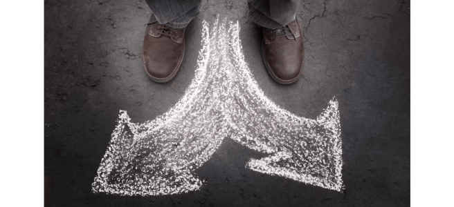 Photo from above of a person standing before a chalked arrow that points both to the left and to the right.